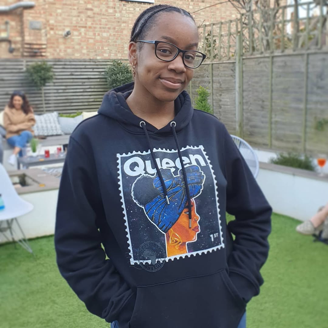 black woman wearing a hoodie with a 'Queen' design in an outdoor setting